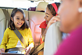 Sisters riding in back seat of car with tablet