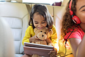 Cute girl with teddy bear using tablet in back seat of car