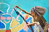 Senior woman painting vibrant mural on wall