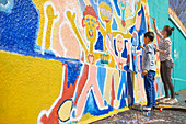 Mother and son volunteers painting vibrant mural on wall