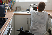 Young woman in wheelchair filling kettle