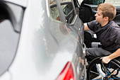 Young woman in wheelchair opening car door