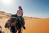 Woman riding camel in desert, Sahara, Morocco