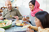 Happy woman in hijab eating dinner with family at table