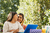 Happy mother and daughter using laptop on patio