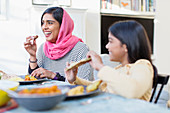Happy mother in hijab and daughter eating dinner