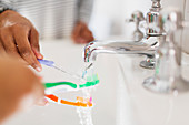 Close up family rinsing toothbrushes in bathroom sink