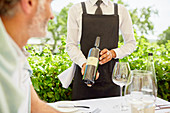 Wine steward showing wine bottle to man dining on patio