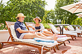 Mature couple relaxing on lounge chairs at poolside