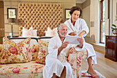 Mature couple in spa bathrobes using digital tablet