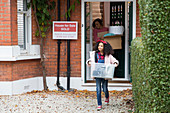 Girl moving out of house, carrying belongings in driveway