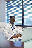 Male doctor working at laptop in doctors office