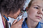Pediatrician examining ear of girl patient