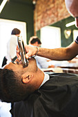 Male barber shaving face of customer in barbershop