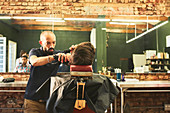 Male barber giving customer a haircut in barbershop
