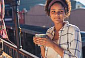 Smiling young woman drinking coffee on sunny balcony