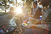 Family eating at sunny campsite campfire in woods