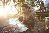 Man blowing on campfire in sunny woods