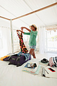 Happy woman unpacking suitcase in beach house bedroom