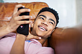 Smiling teenage boy using smart phone on sofa