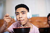 Teenage boy with headphones eating noodles