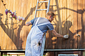 Male worker on ladder staining wood siding