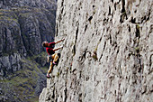 Male rock climber scaling rock face, looking up