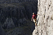 Male rock climber scaling tall rock face