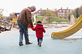 Grandfather walking with toddler grandson at playground