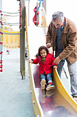 Grandfather playing with toddler on slide