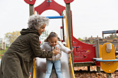 Grandmother playing with granddaughter on playground slide