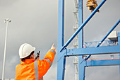Dock worker with walkie-talkie directing crane at shipyard