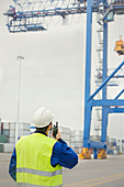 Dock worker with walkie-talkie watching crane at shipyard