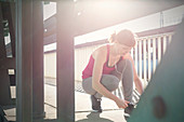 Young female runner tying shoe on sunny urban sidewalk