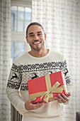 Portrait young man in Christmas sweater holding gift