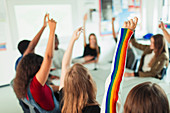 Students with arms raised, asking questions in classroom