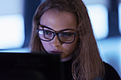 Focused teenage girl in eyeglasses using laptop