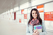 Portrait young woman with books standing in urban corridor