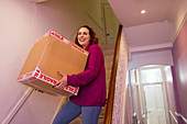 Woman moving house, carrying cardboard box on stairs