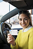 Portrait happy woman holding new drivers license in car