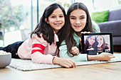 Sisters using digital tablet camera on living room floor