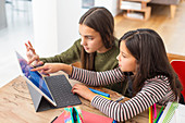 Sisters doing homework, sharing digital tablet at table