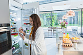 Woman with digital tablet at refrigerator in kitchen
