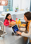Daughter watching mother using digital tablet in kitchen