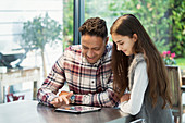 Father and daughter using digital tablet in kitchen