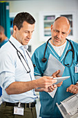 Male doctors consulting, using digital tablet in hospital