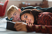Teenage couple using smart phone, laying on bed