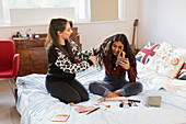 Teenage girls applying makeup and brushing hair on bed