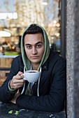 Portrait young man in hoody drinking cappuccino