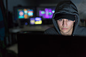 Male hacker in hoody using computer in dark room